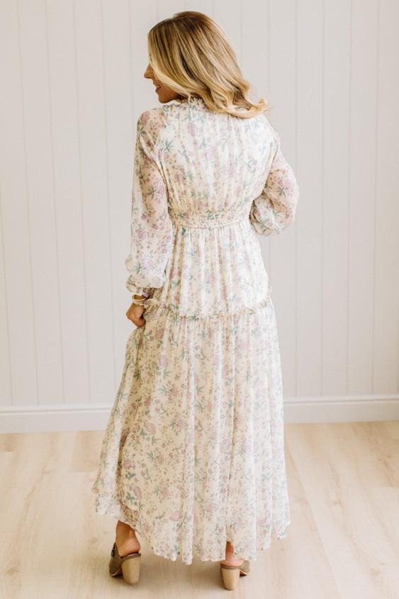 Woman wearing a cream floral dress against a white paneled wall.