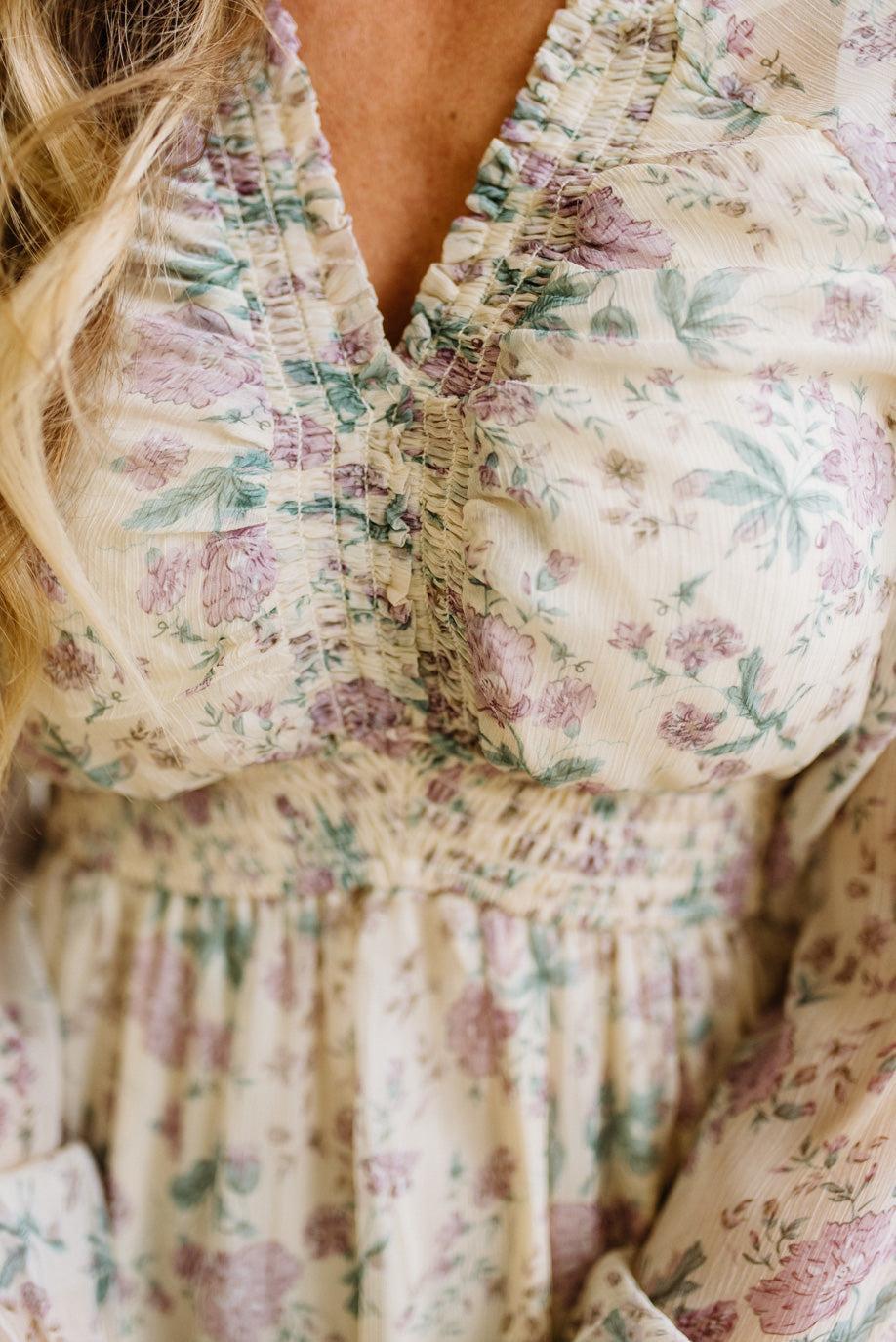 Woman wearing a cream floral dress against a white paneled wall.