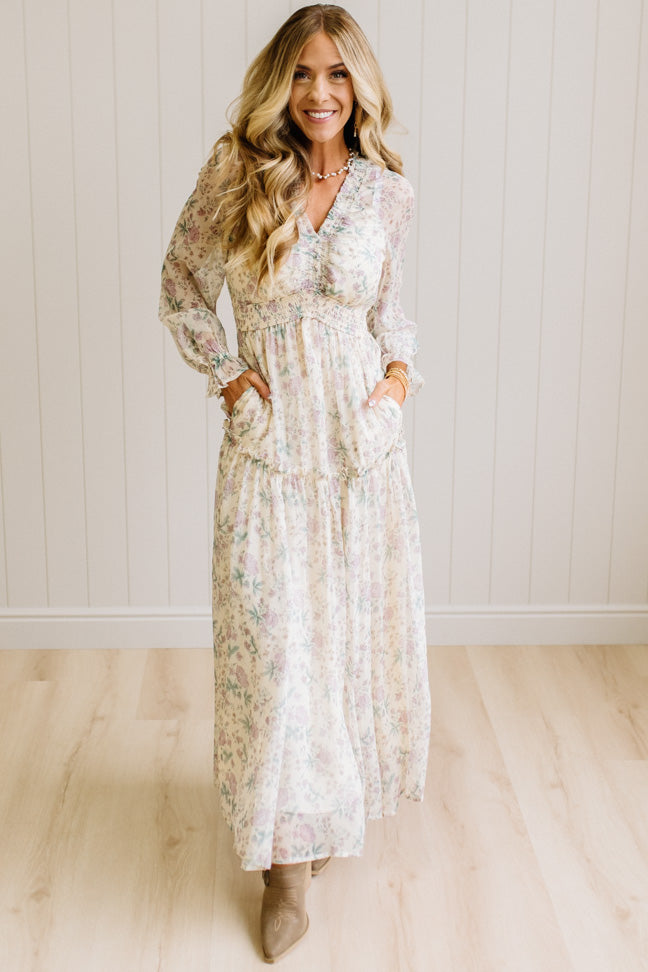 Woman wearing a cream floral dress against a white paneled wall.
