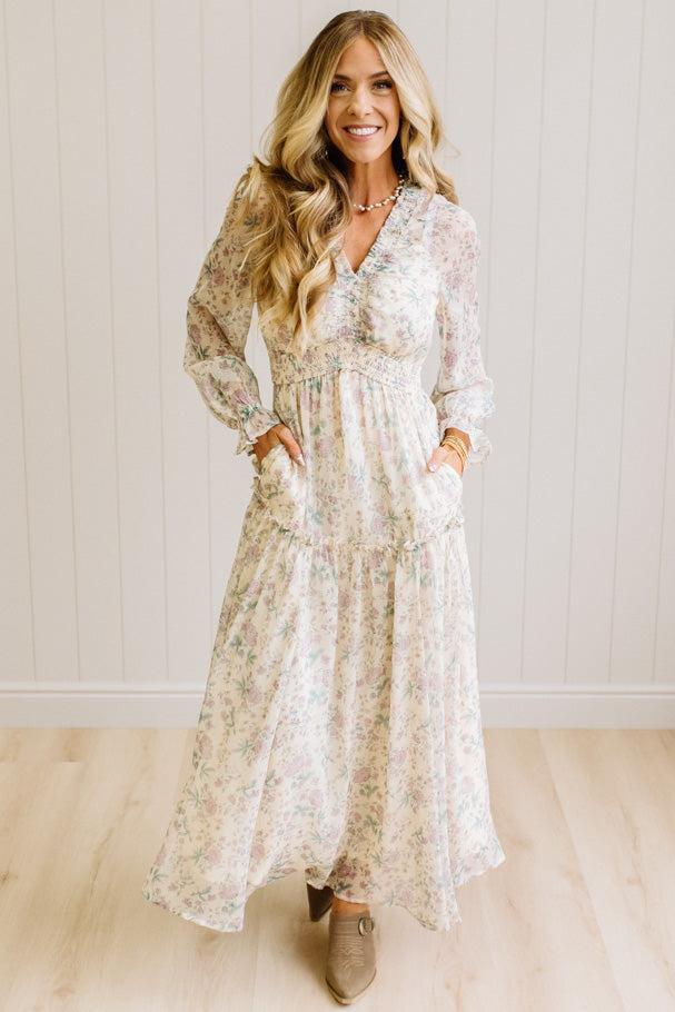 Woman wearing a cream floral dress against a white paneled wall.