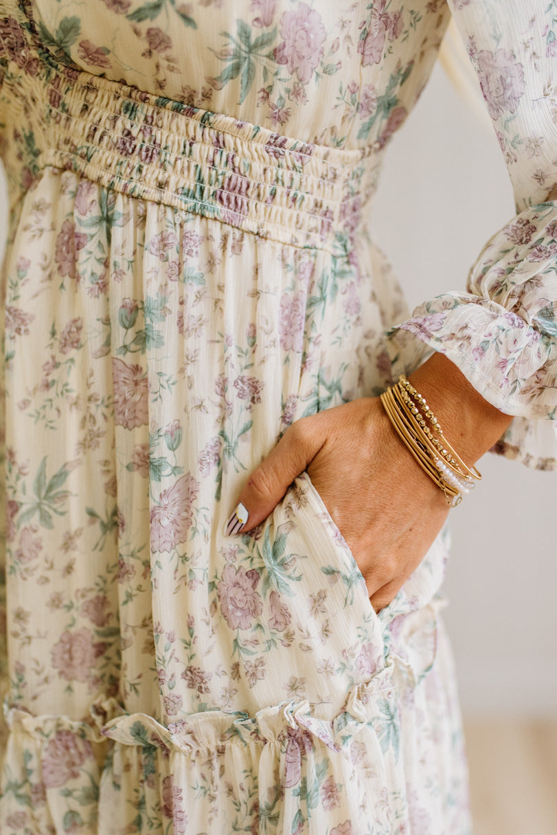 Woman wearing a cream floral dress against a white paneled wall.