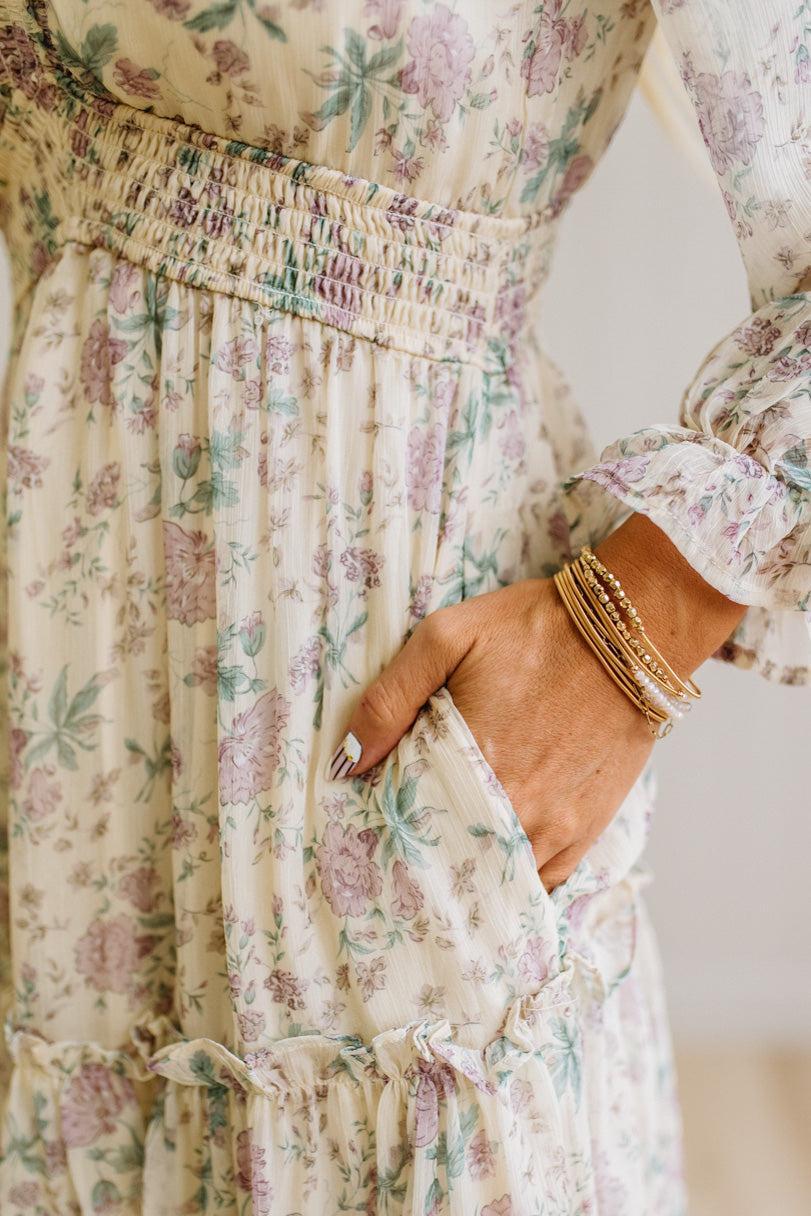 Woman wearing a cream floral dress against a white paneled wall.