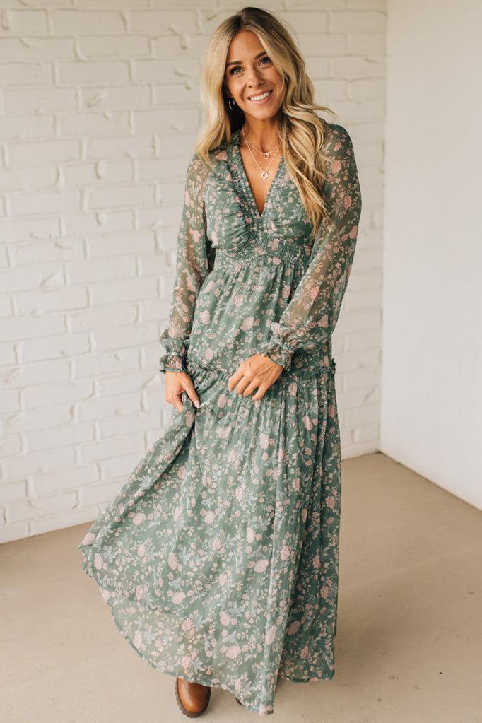 Woman wearing a green floral dress against a white brick wall.