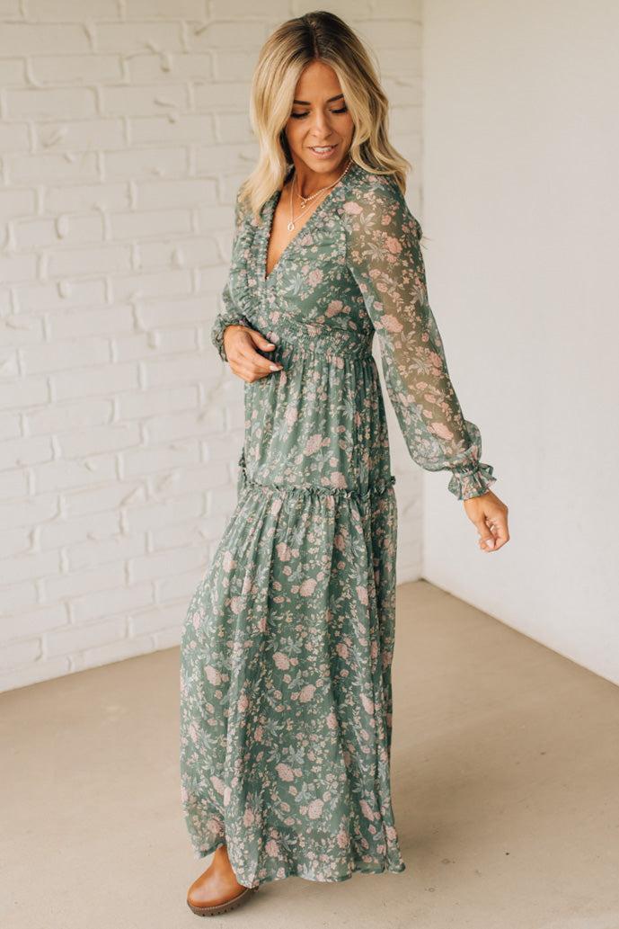 Woman wearing a green floral dress against a white brick wall.