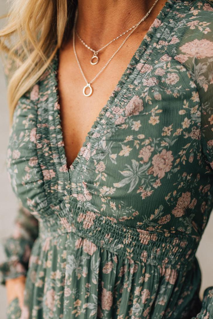 Green floral dress with a plunging neckline and layered necklaces.