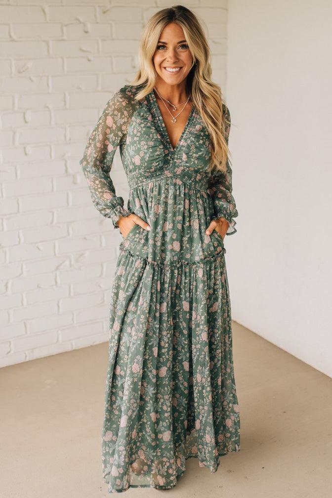 Woman wearing a green floral dress against a white brick wall.