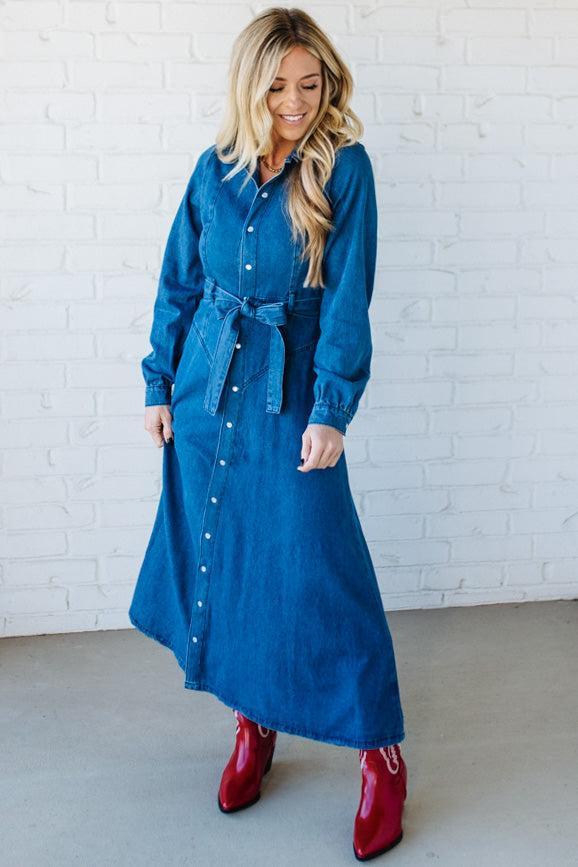 Woman wearing a blue denim dress with red boots against a white brick wall.
