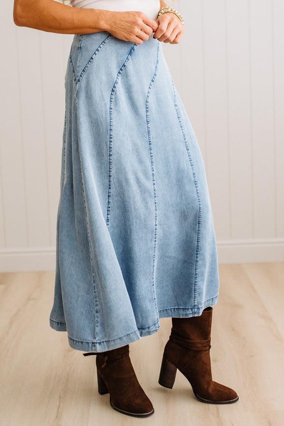 Blonde woman in a studio with light floor and a paneled wall behind, wearing a Denim Diagonal Line Detail Midi Skirt.