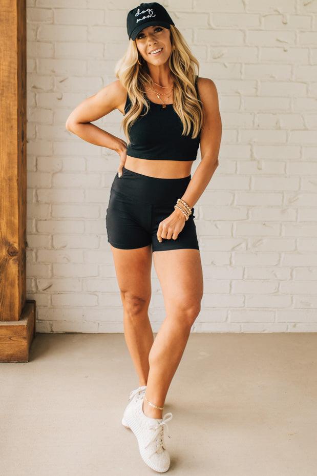 Blonde woman wearing a black tank and black high thigh biker shorts in solid black.