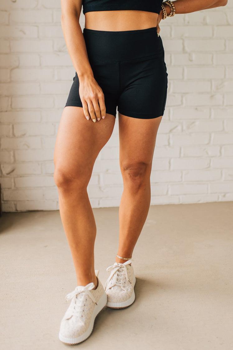 Blonde woman wearing a black tank and black high thigh biker shorts in solid black.
