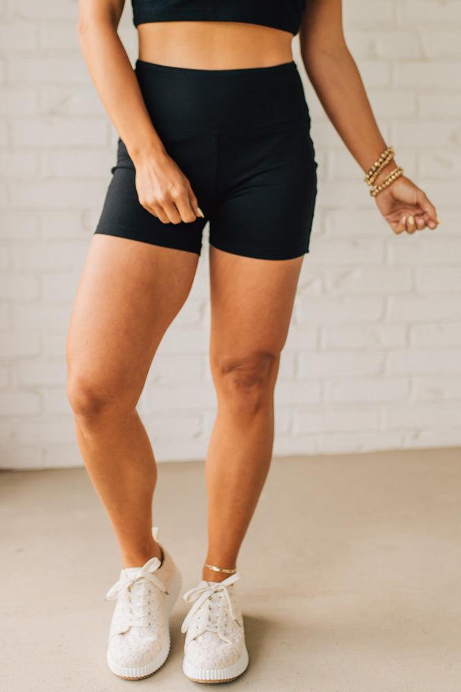 Blonde woman wearing a black tank and black high thigh biker shorts in solid black.