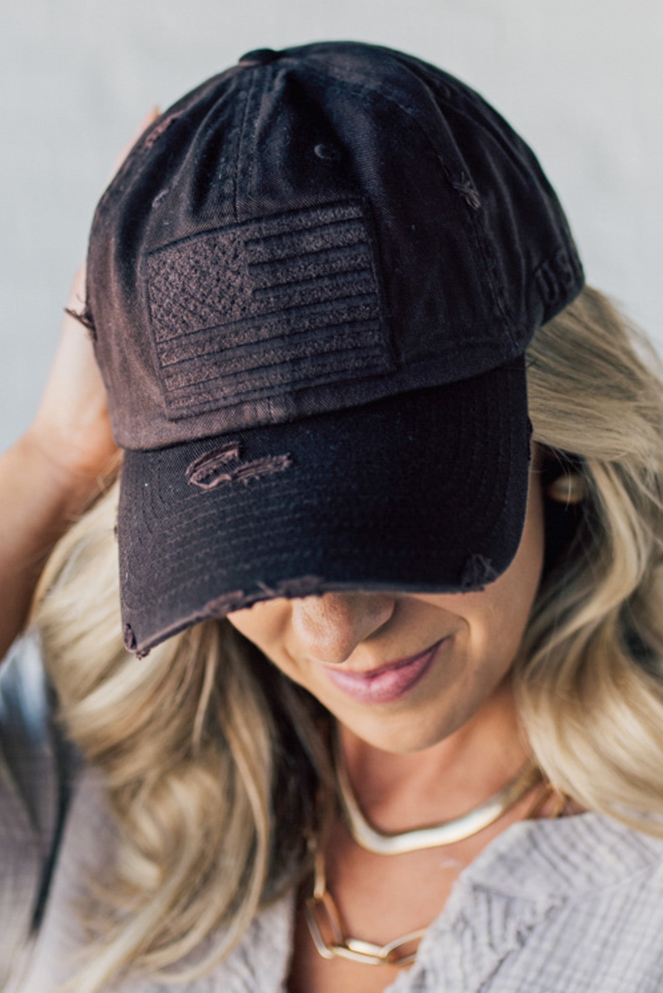 Blonde woman wearing a single color distressed american flag hat.