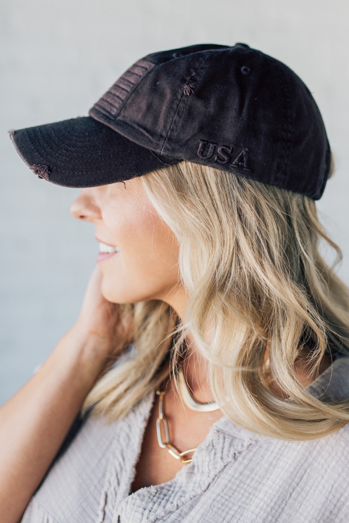 Blonde woman wearing a single color distressed american flag hat.