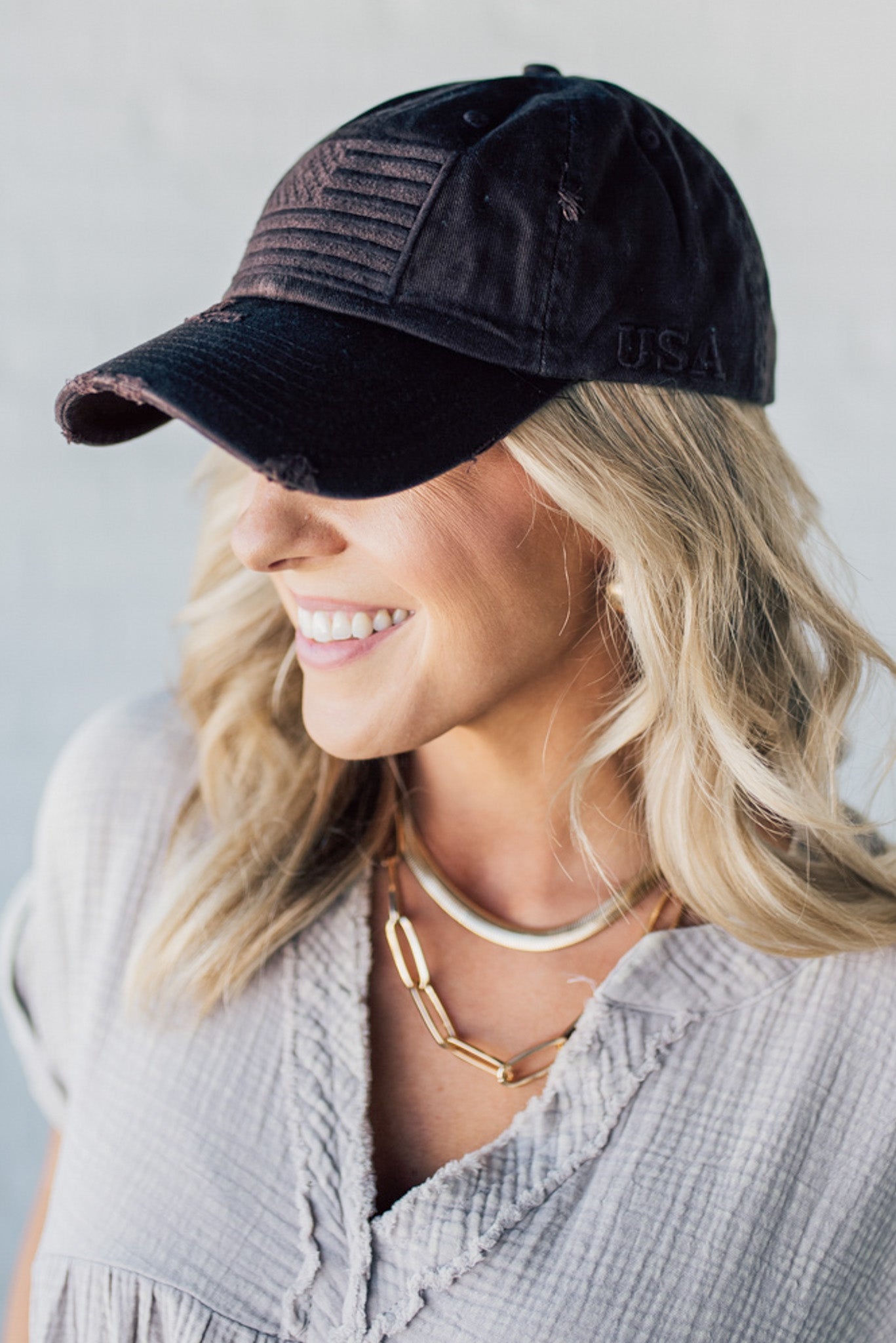 Blonde woman wearing a single color distressed american flag hat.