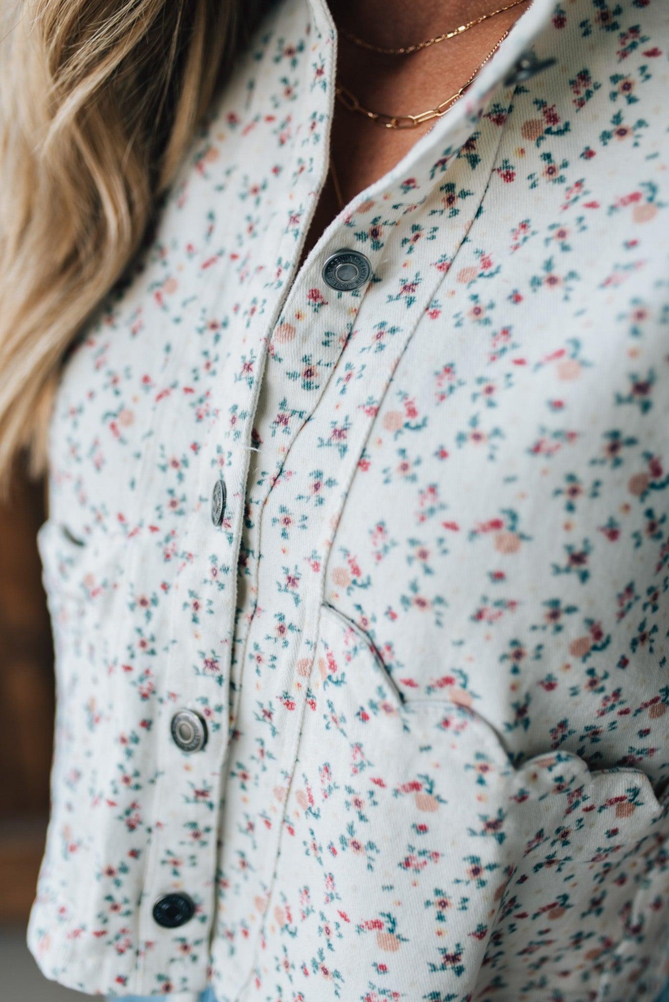 BLONDE WOMAN WEARING A DITSY FLORAL PRINT SCALLOP EDGE DETAILED DENIM CROP VEST.