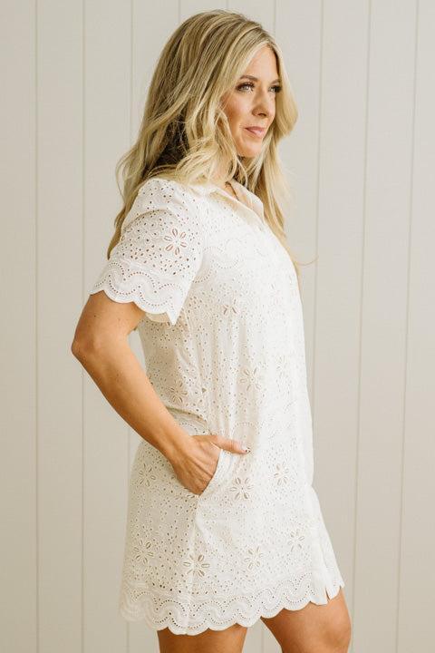 Blonde woman wearing a button front collared shift dress with scalloped edges, and all over eyelet lace embroidery in cream.