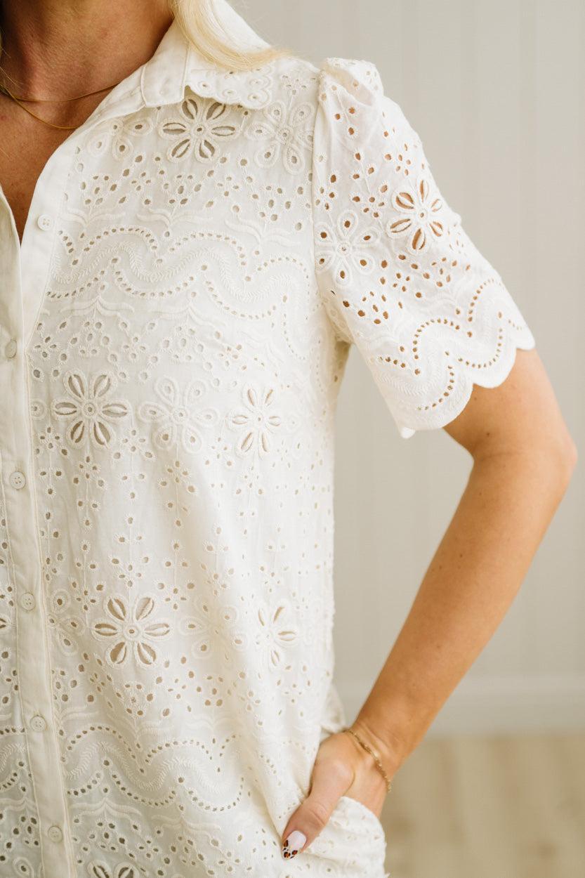 Blonde woman wearing a button front collared shift dress with scalloped edges, and all over eyelet lace embroidery in cream.