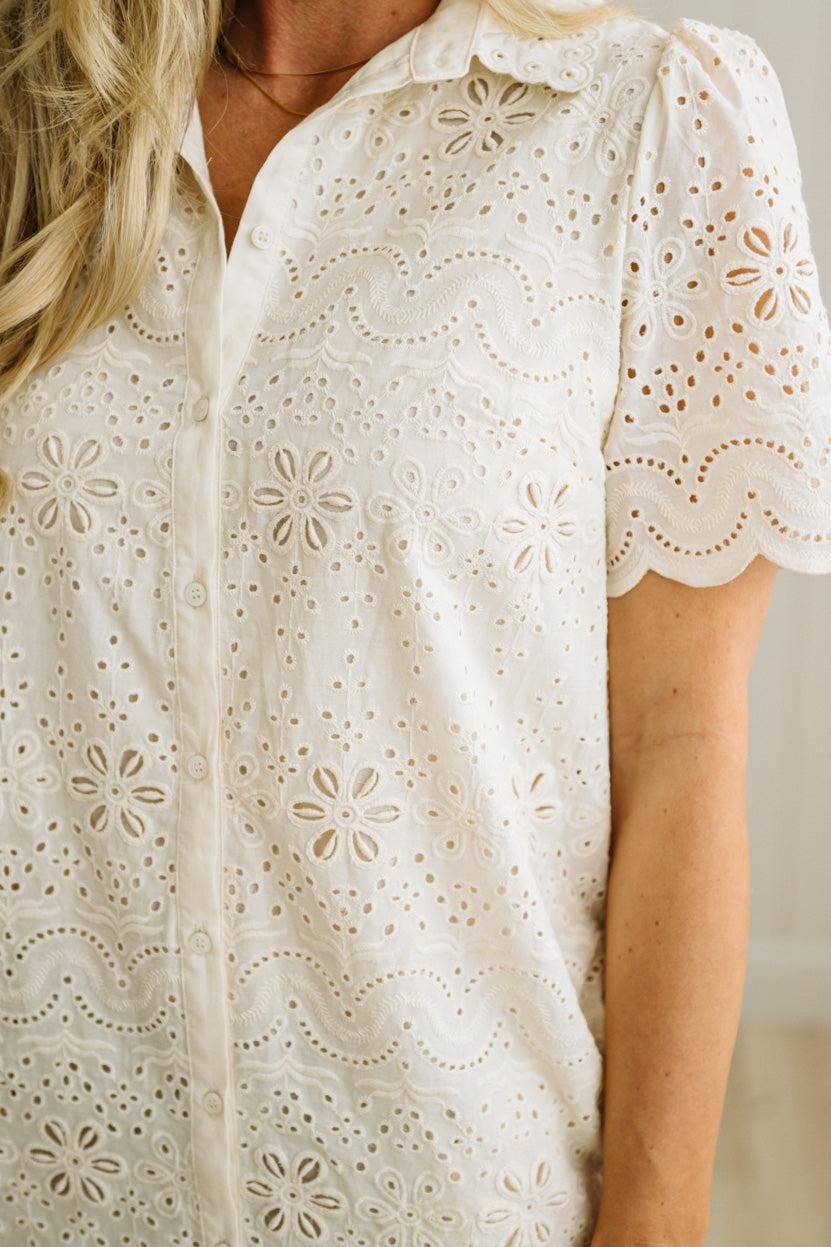 Blonde woman wearing a button front collared shift dress with scalloped edges, and all over eyelet lace embroidery in cream.
