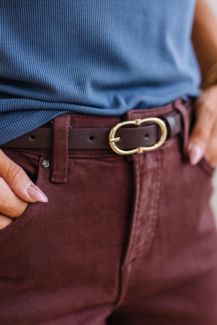 Close-up of a person wearing a blue shirt, jeans, and a brown belt with a gold buckle.