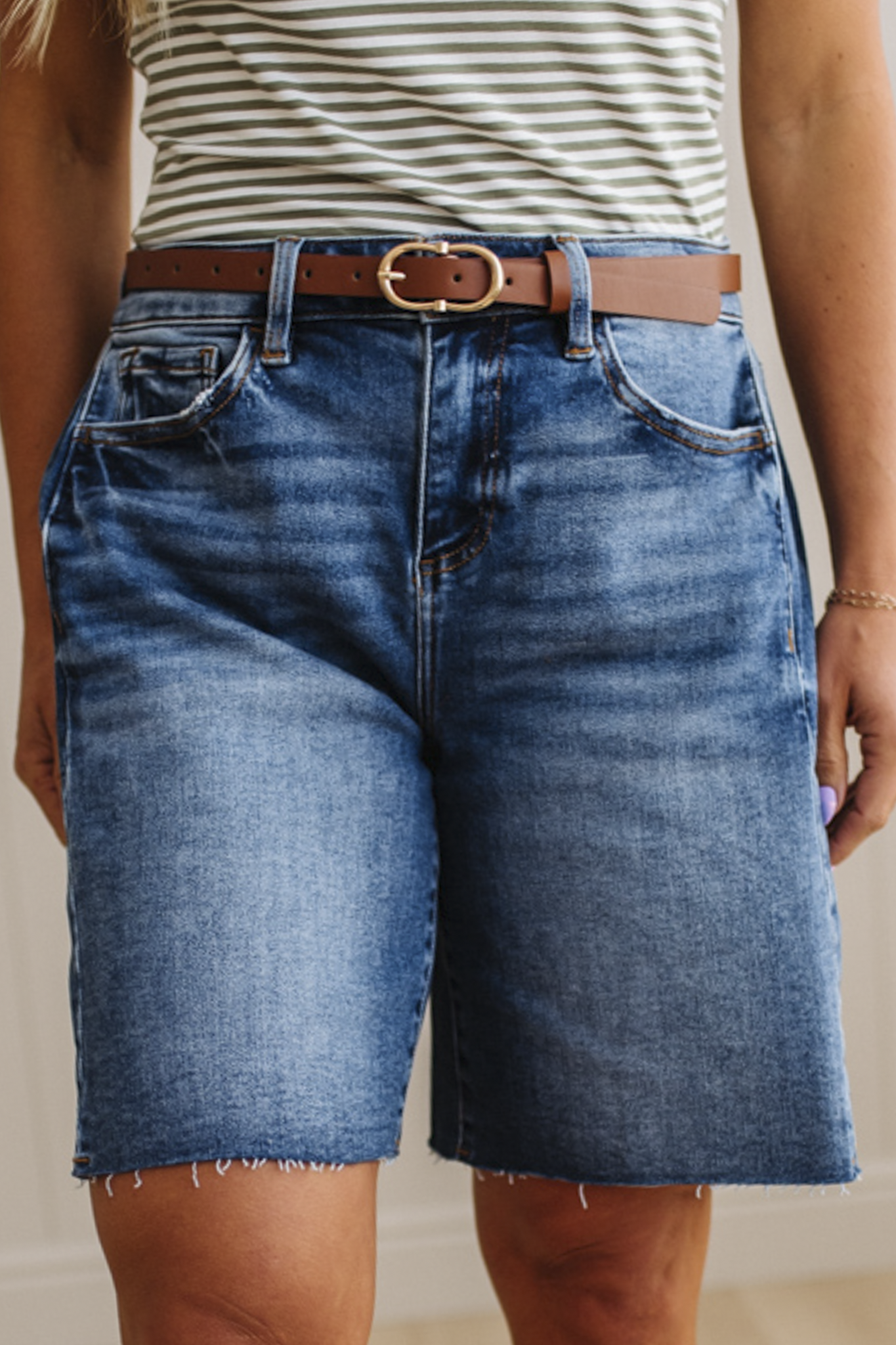 Person wearing blue denim shorts with a brown belt and striped shirt.