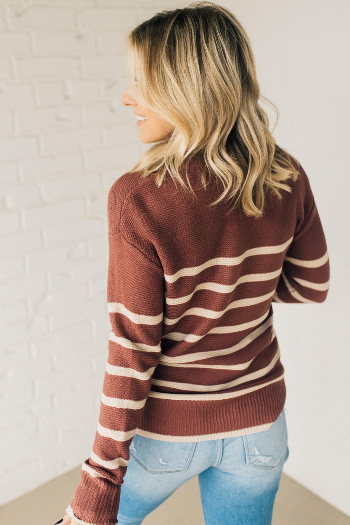 A woman smiling while wearing a beige and red/brown striped sweater with a round neckline and long sleeves.