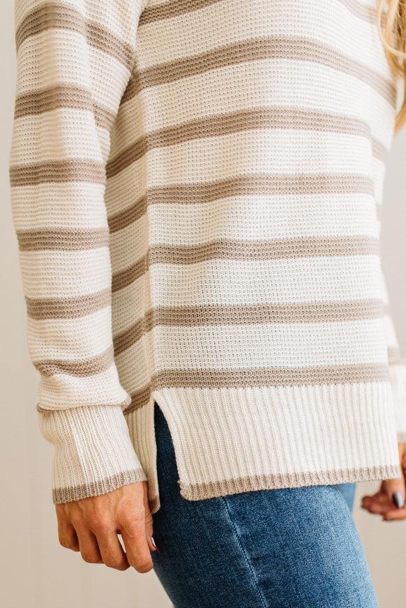 Close-up of a person wearing a striped sweater and blue jeans against a neutral background