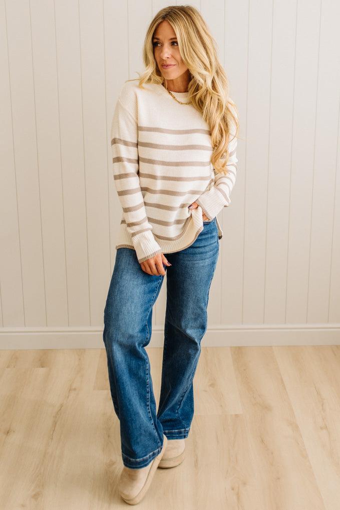Woman wearing a striped sweater and blue jeans against a white wall.