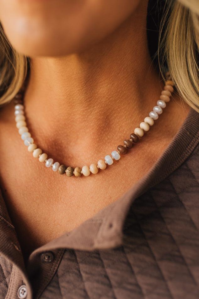 Close-up of a person wearing a beaded necklace with a neutral background