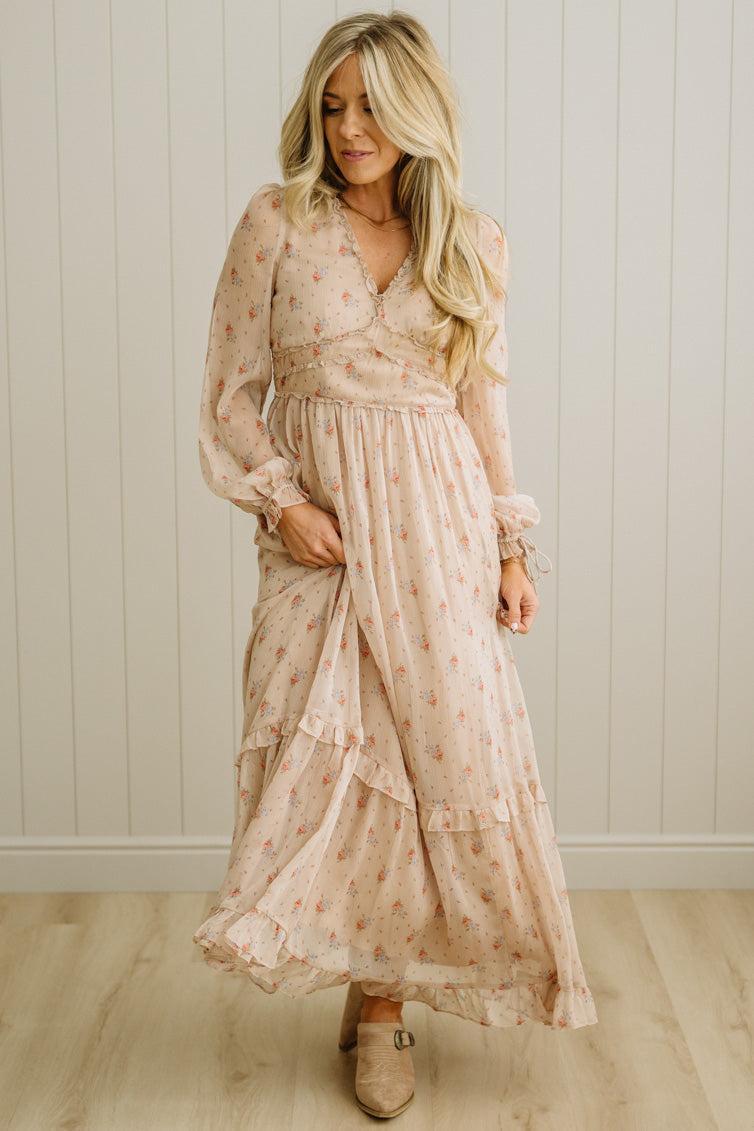 Woman wearing a floral dress standing against a white paneled wall.