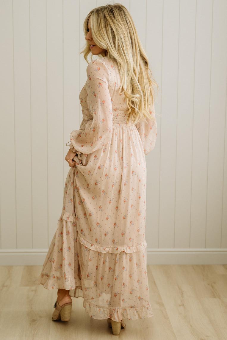 Woman wearing a long, light-colored dress with a subtle pattern against a white paneled wall.