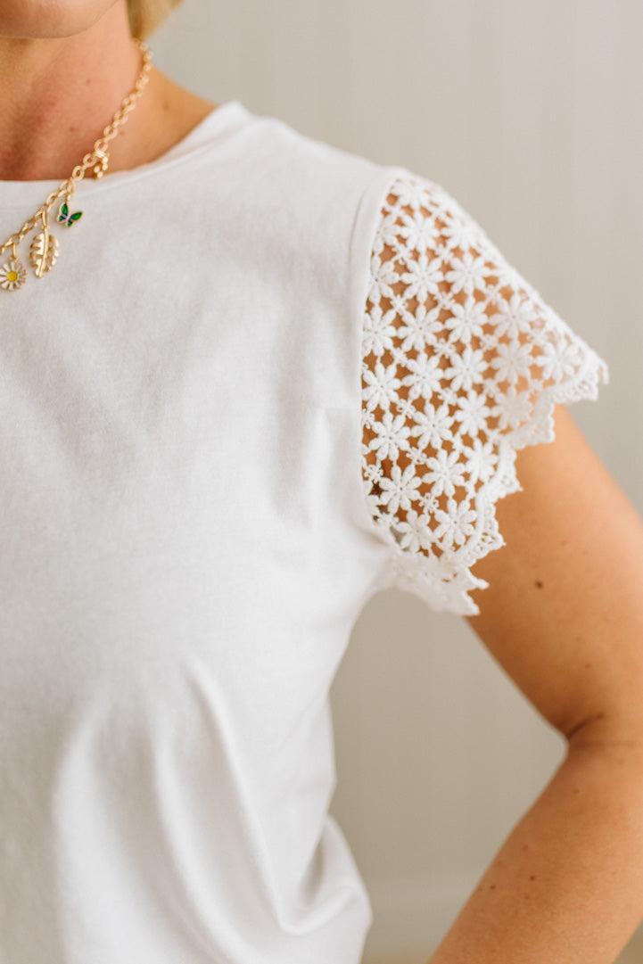 White blouse with lace sleeves worn by a person, on a neutral background