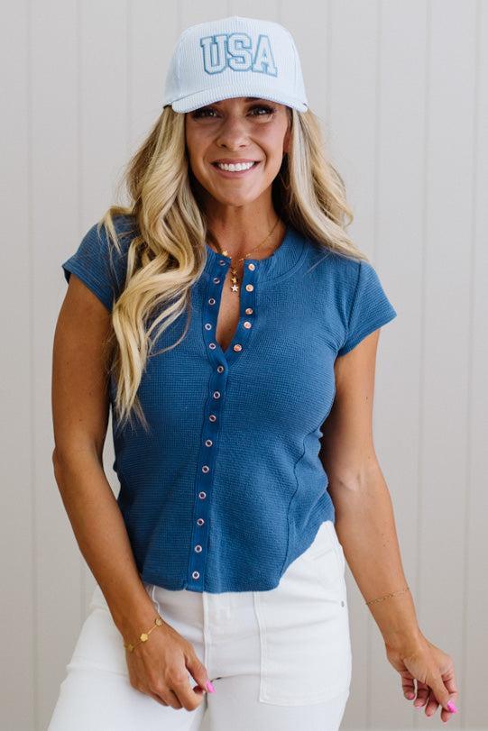 Woman wearing a blue top and white cap with 'USA' text against a neutral background