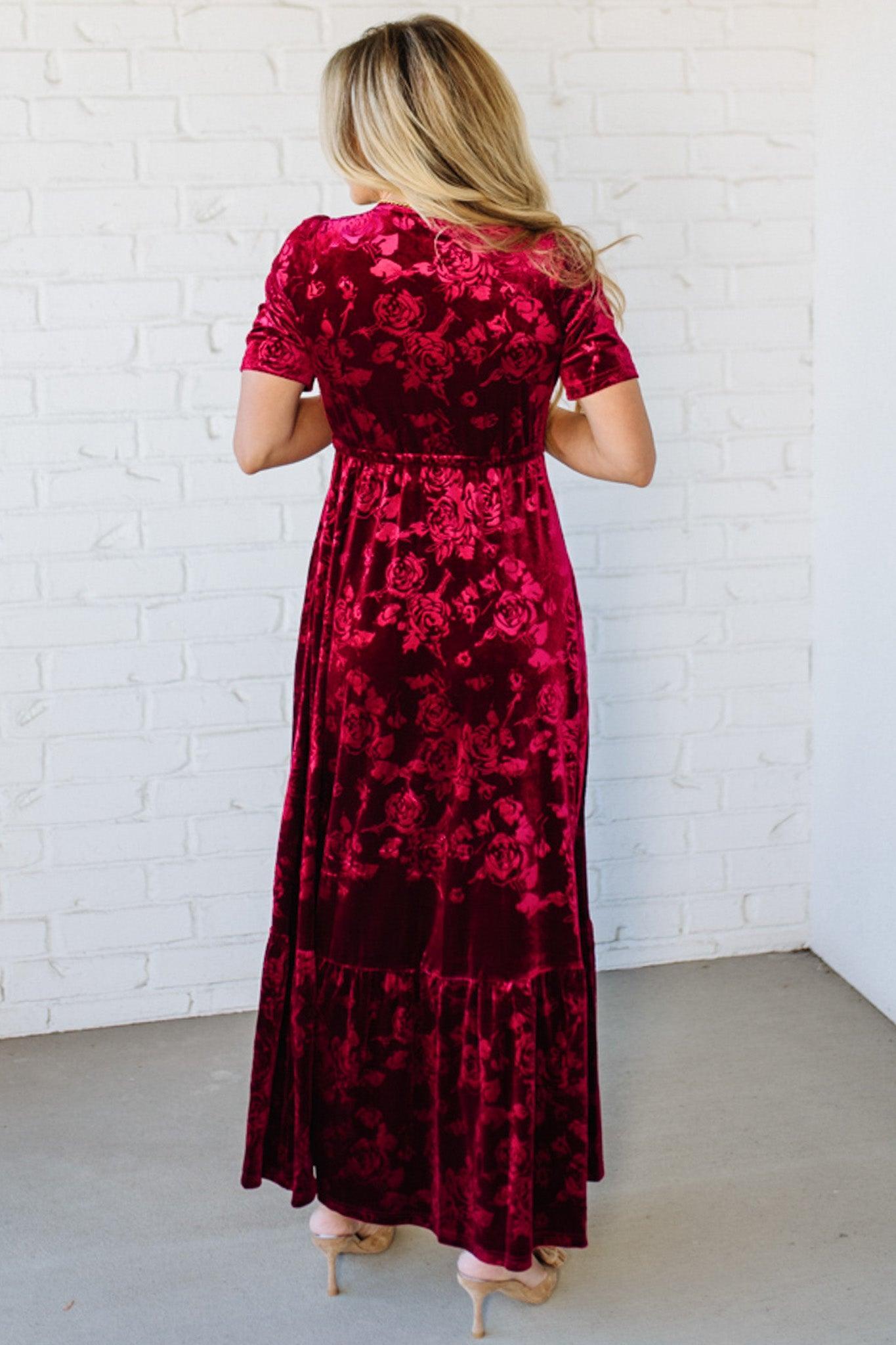 Woman wearing a red floral dress against a white brick wall.