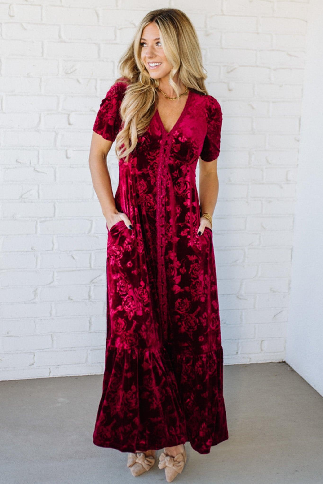 Woman wearing a red floral dress against a white brick wall.