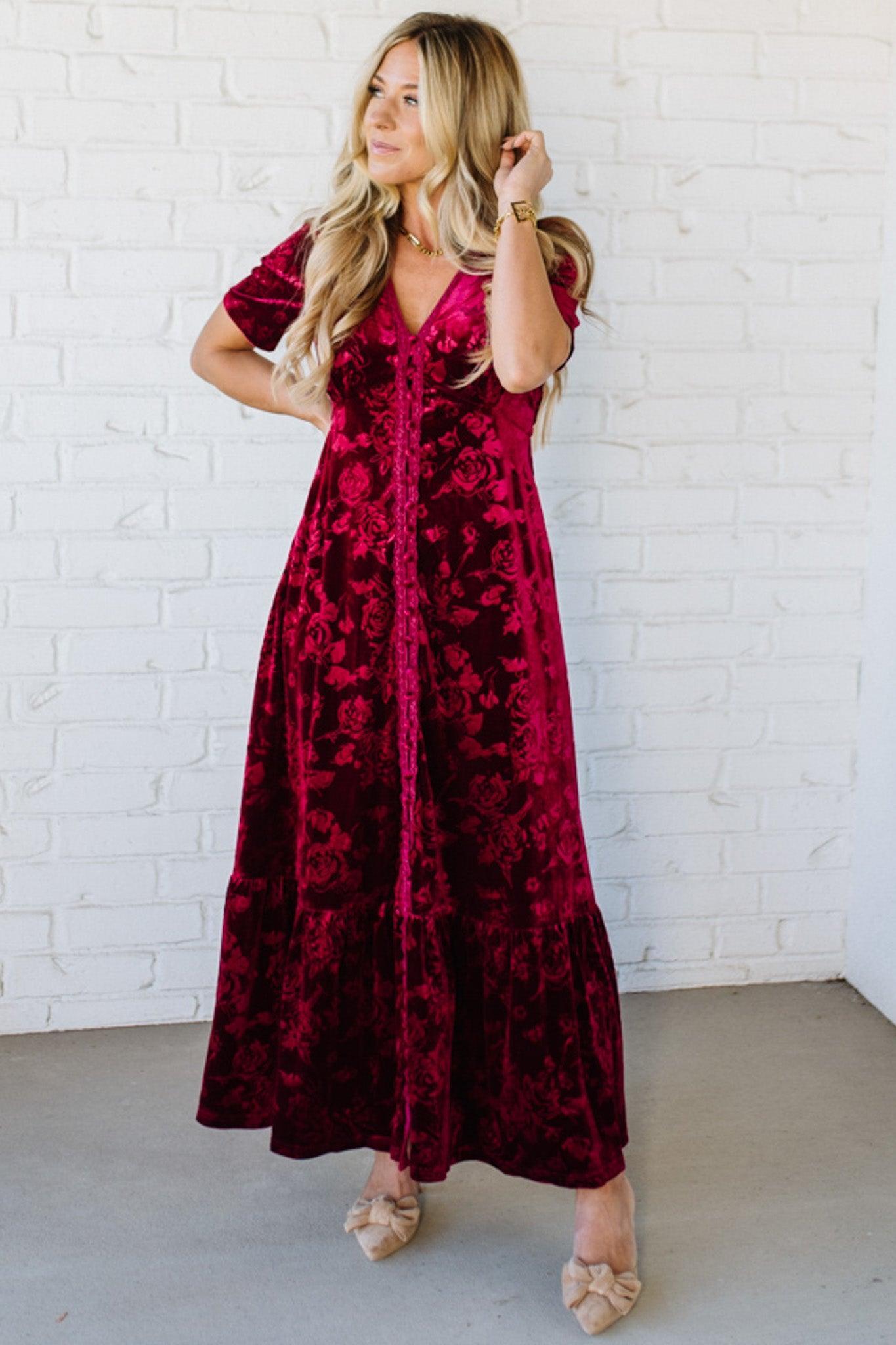 Woman wearing a red floral dress against a white brick wall.