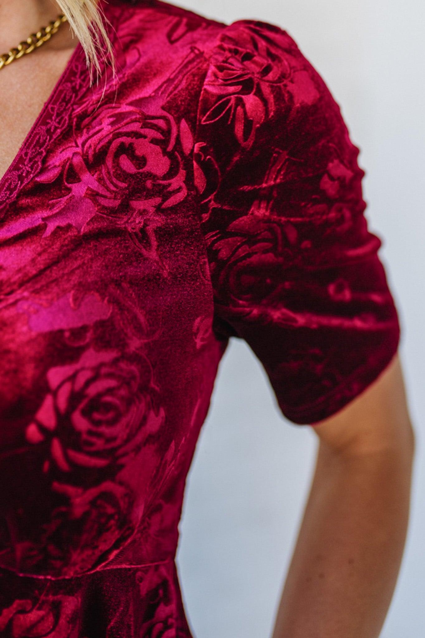 Close-up of a red velvet dress with floral patterns on a plain background