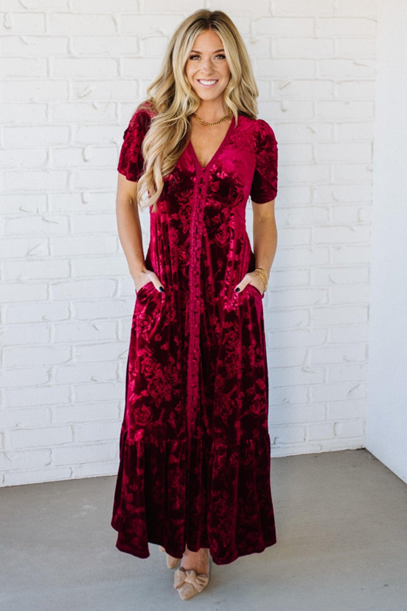 Woman wearing a red velvet dress against a white brick wall.