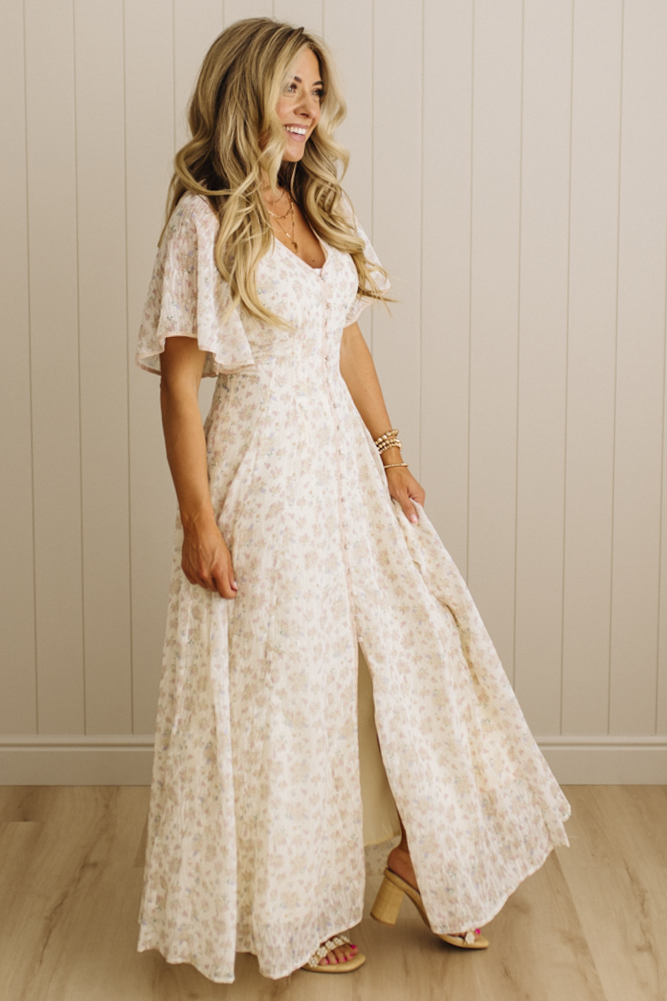 Woman wearing a white lace dress standing against a beige wall.