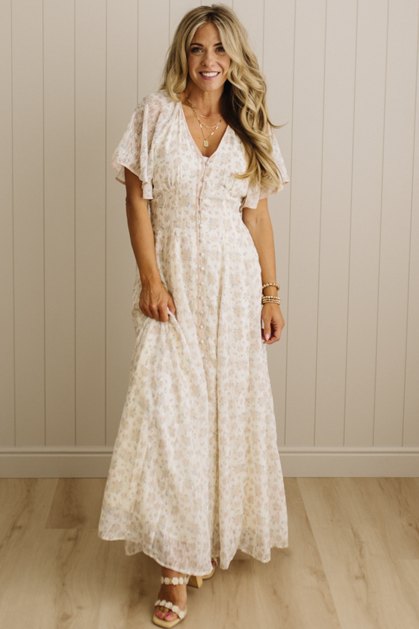 Woman wearing a white lace dress standing against a beige wall.