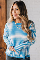 BLONDE WOMAN MODELING A LONG SLEEVE STRIPED LIGHTWEIGHT SWEATER WITH RIBBED SOLID COLORED NECKLINE AND SLEEVE CUFFS