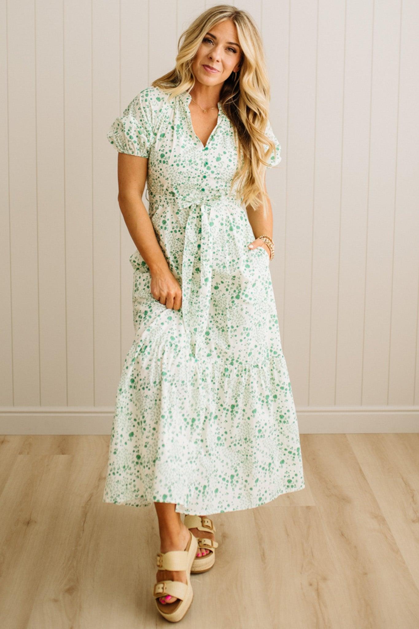 Woman wearing a floral dress standing against a beige wall.