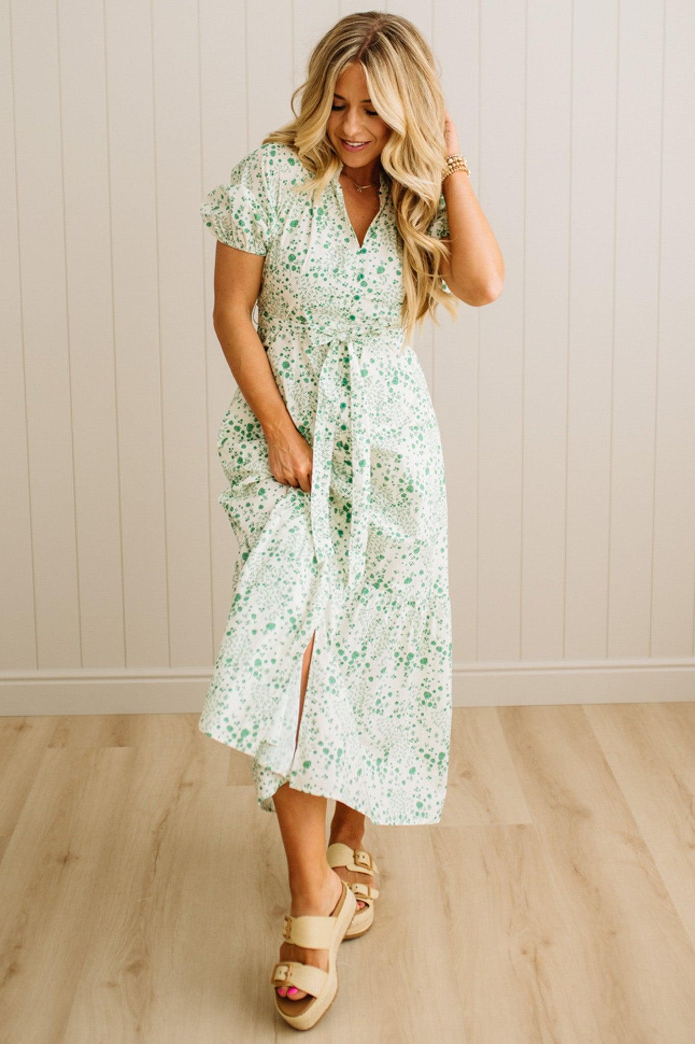 Woman wearing a floral dress standing against a plain wall.