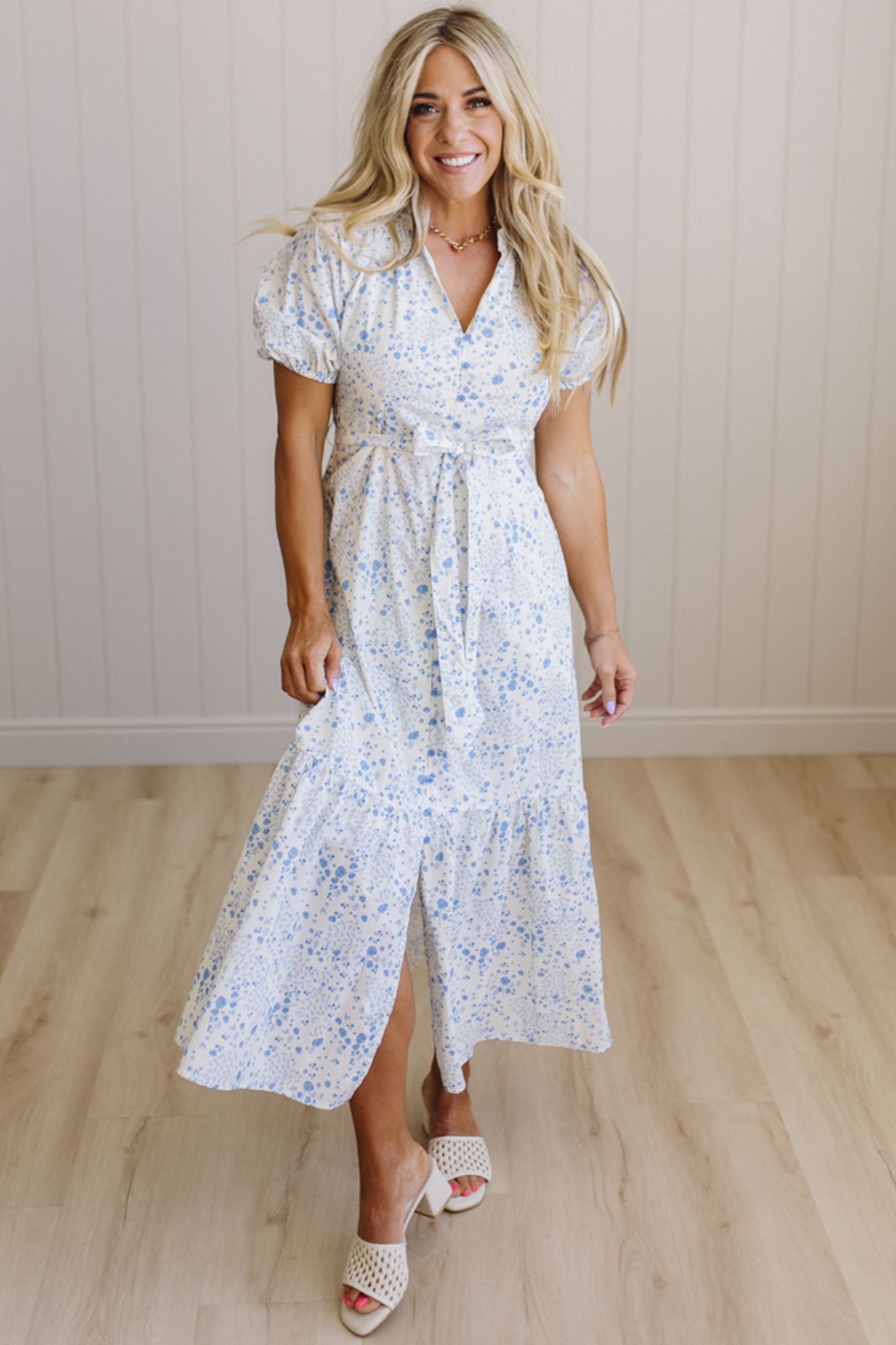 Woman wearing a white floral dress standing on a wooden floor with a light-colored wall background