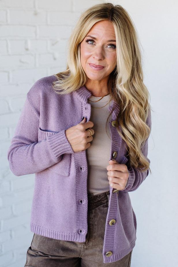 Woman wearing a purple cardigan against a white brick wall