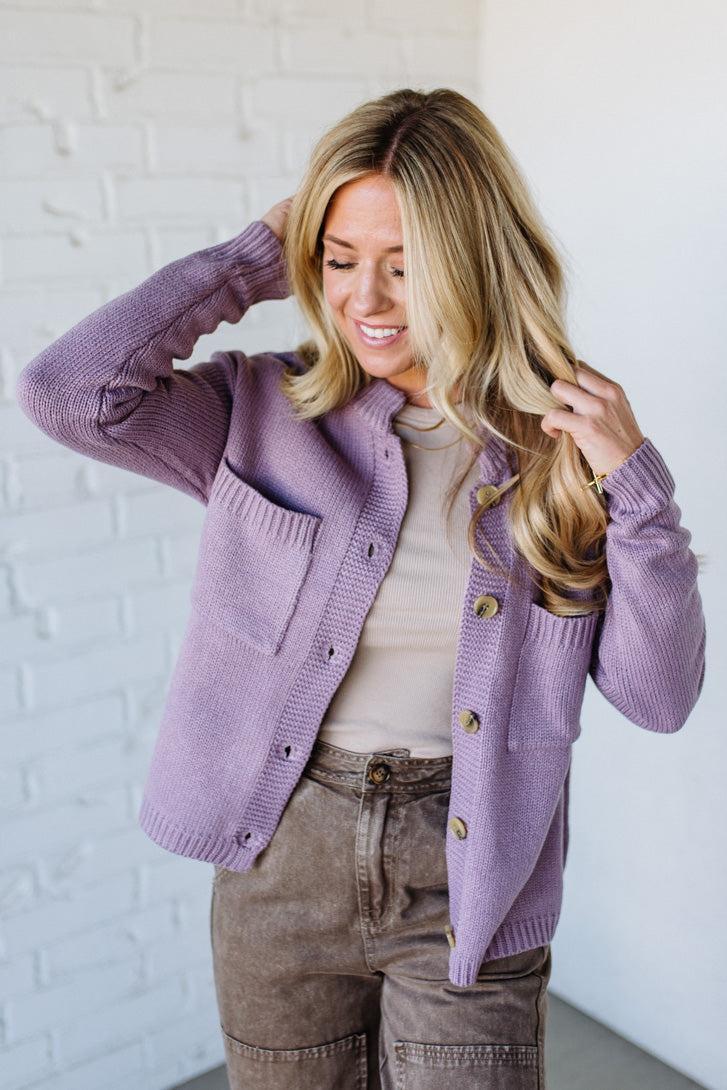 Woman wearing a purple cardigan with a white brick wall background