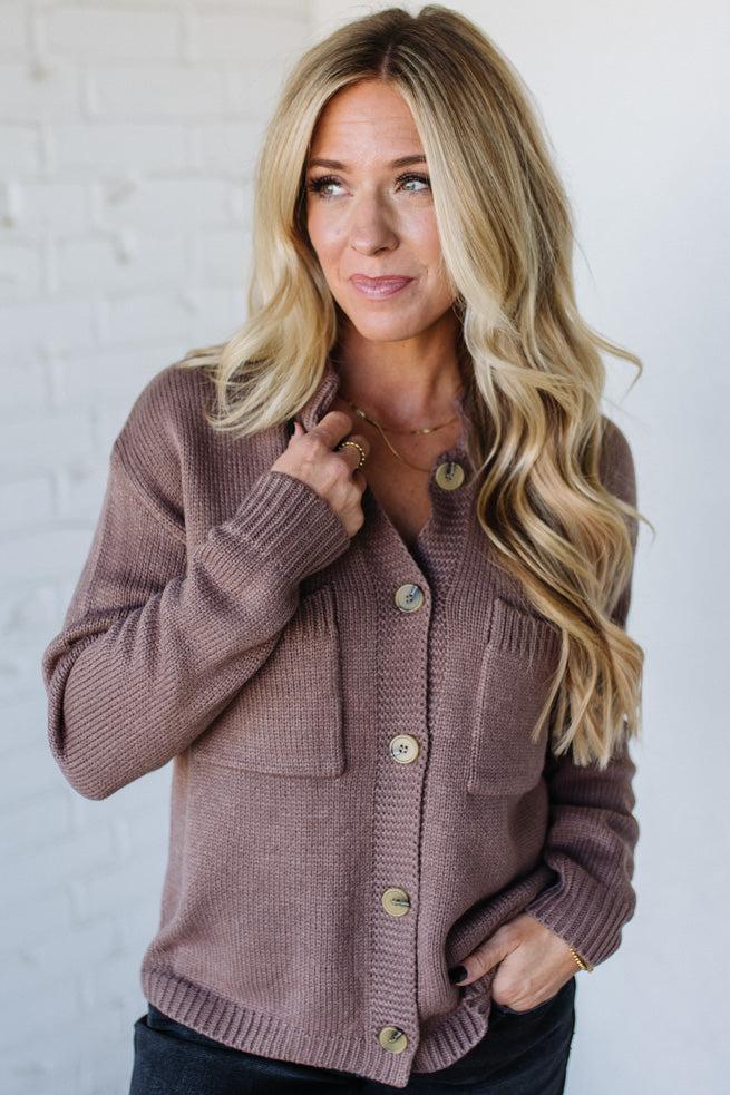 Woman wearing a brown cardigan against a white brick wall