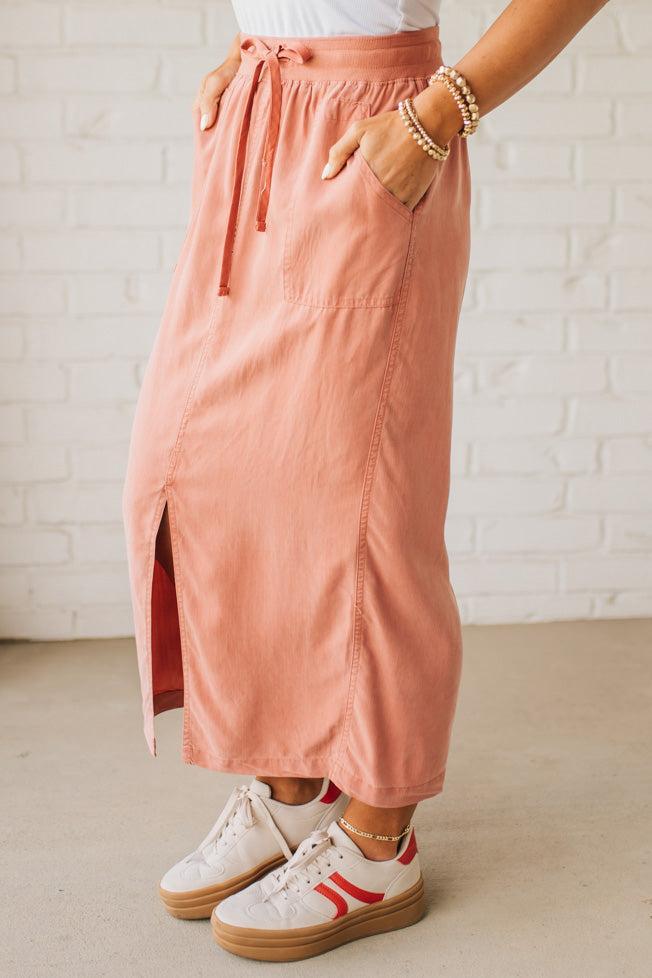 Blonde woman in a hat wearing a white tank top and sneakers with a tencel cargo midi skirt with a center slit at the front.