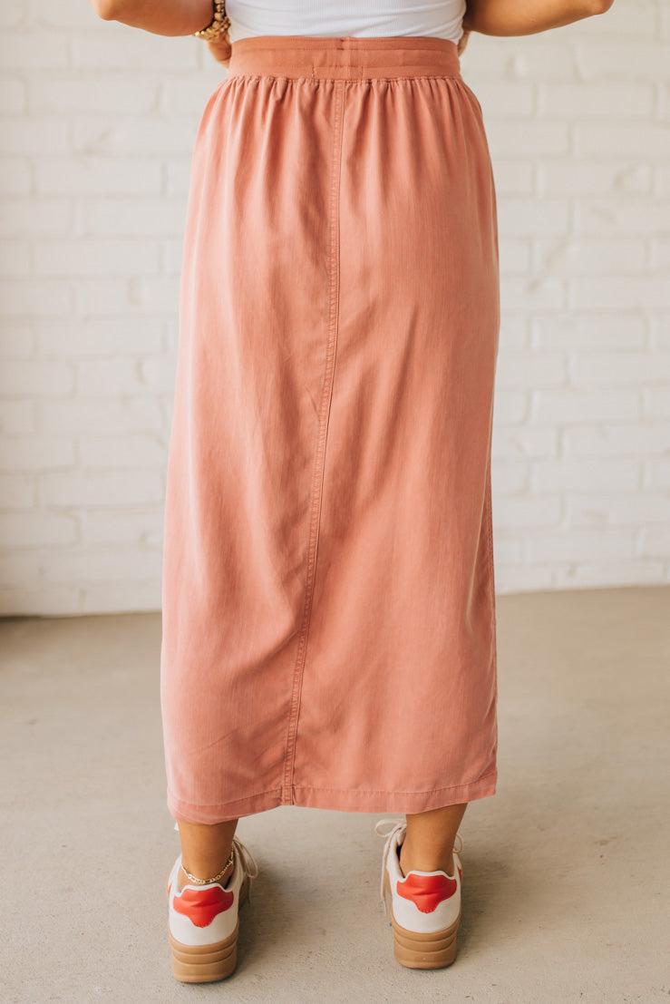 Blonde woman in a hat wearing a white tank top and sneakers with a tencel cargo midi skirt with a center slit at the front.