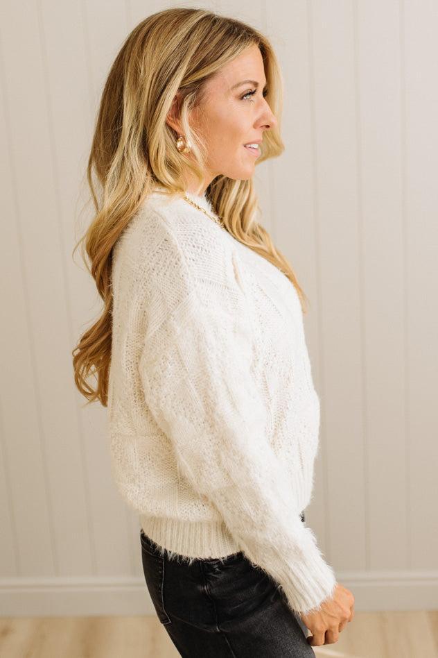 Woman wearing a white cable knit sweater against a neutral background