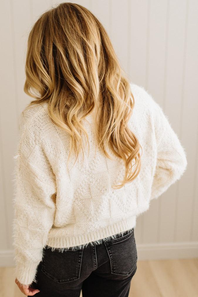 Person wearing a white textured sweater and black pants against a neutral background